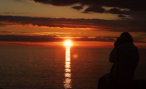 Silhouette woman looking at sea against sky during sunset