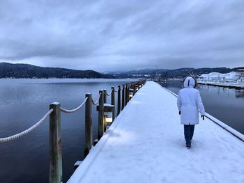 Rear view of woman walking on snow covered pier over frozen lake during winter