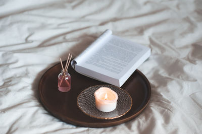 Home liquid fragrance in glass bottle with wooden sticks and scent candle with open paper book