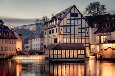 Buildings by river against sky at dusk