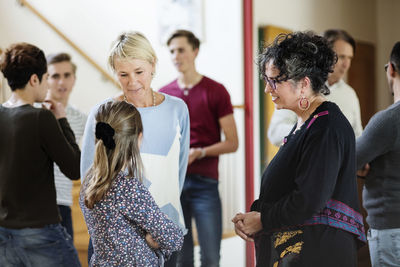 Mother talking to daughter against friends and family standing in living room