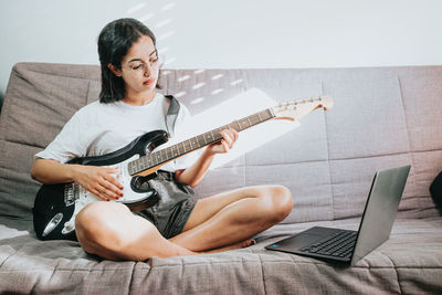 Young man playing guitar while sitting on sofa at home