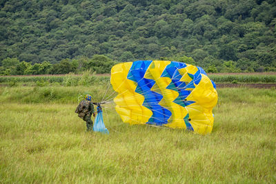 Army soldier with parachute walking on field against trees