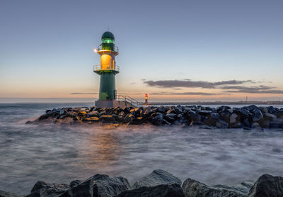 Lighthouse by sea against sky during sunset