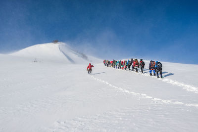 People on snowcapped mountain against blue sky