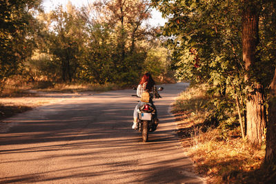 Rear view of woman riding motorcycle on road