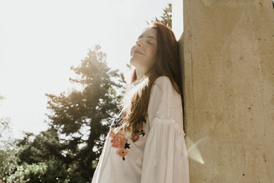 Smiling young woman leaning on wall during sunny day