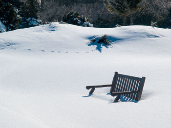 Empty bench on snow covered field during winter