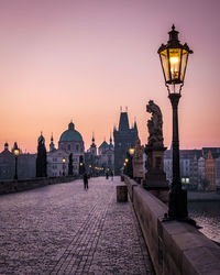 Illuminated street light by building against sky at dusk