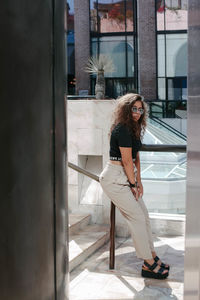 Full length portrait of young woman sitting on railing in city