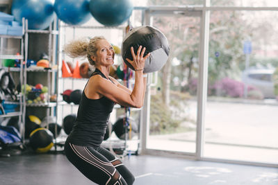 Portrait of smiling woman exercising with medicine ball while at gym