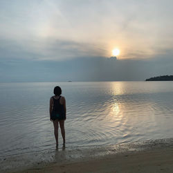 Rear view of man on beach against sky during sunset