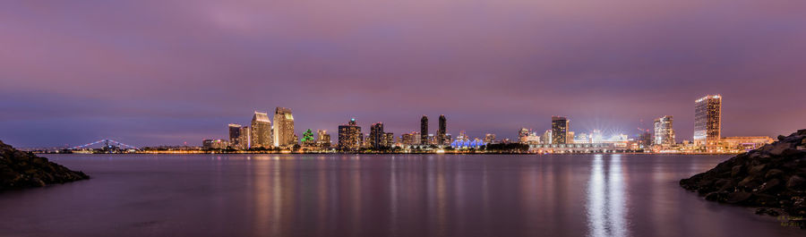 Illuminated buildings by sea against sky at night