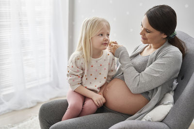 Pregnant woman with daughter sitting at home