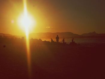 Silhouette people on shore against sunset sky