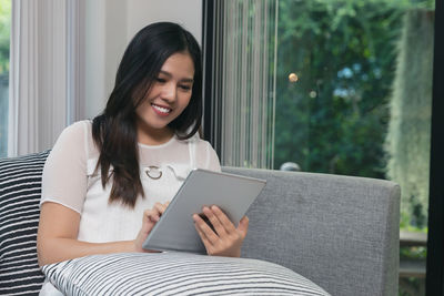 Young woman using digital tablet while sitting on sofa at home