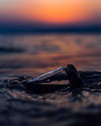 Close-up of bottle in sea during sunset