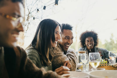 Cheerful male and female friends sitting together at dining table in patio