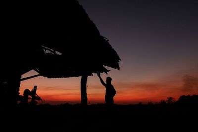 Silhouette man standing on field against sky during sunset