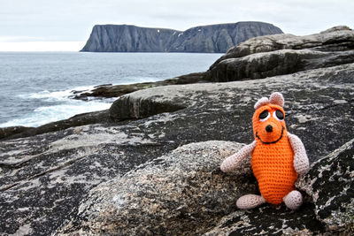 Toy on rock formation by sea against sky