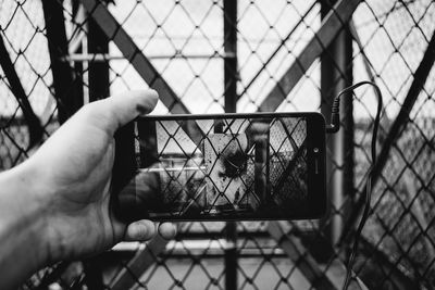 Close-up of cropped hand photographing chainlink fence through smart phone