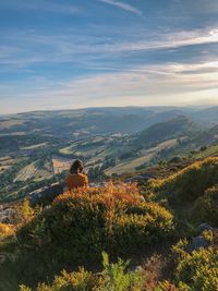 Rear view of woman sitting on mountain against sky