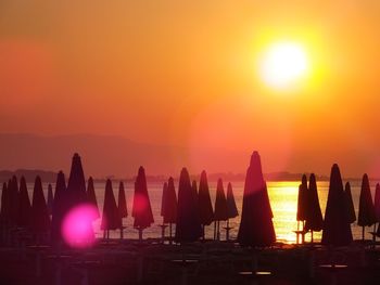 Silhouette people by sea against orange sky during sunset