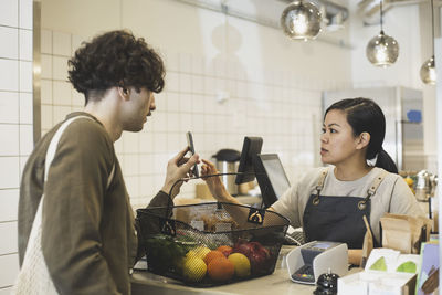 Male customer paying through smart phone to female owner in store