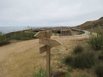 View of arrow sign board on beach against cloudy sky