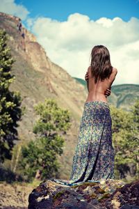 Rear view of shirtless female model wearing skirt against mountains