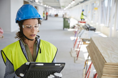 Young female architect in reflective clothing using digital tablet at construction site