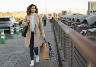 Beautiful young woman holding shopping bags walking on footpath