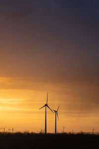 Silhouette wind turbines on field against sky during sunset