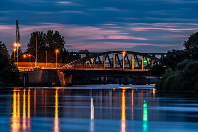 Illuminated bridge over river against sky at night