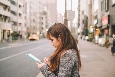 Young woman using mobile phone on road in city