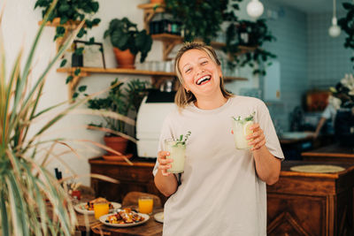 Woman with lemonade laughing at camera while standing in cafe