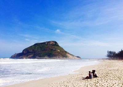 Rear view of people on beach against blue sky