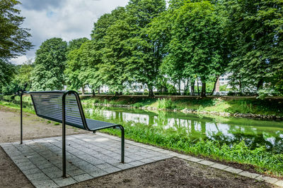 Empty bench by canal against trees at park