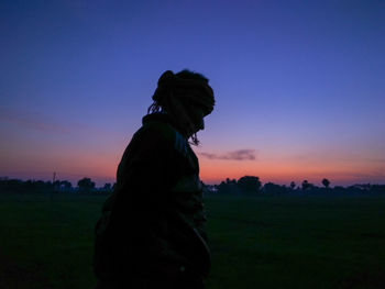 Side view of silhouette man standing on field against sky during sunset