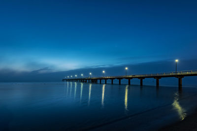 Illuminated bridge over sea against blue sky at night