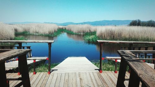 Wooden jetty leading to lake against clear sky