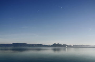 One sail boat in the calm waters of lake trasimeno , italy ,in the background small towns