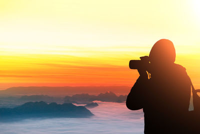 Silhouette man photographing against sky during sunset