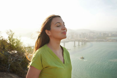Young woman with closed eyes breathing with wind on her face relaxing enjoying sun at sunset