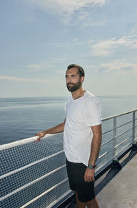 Man standing on railing against sea