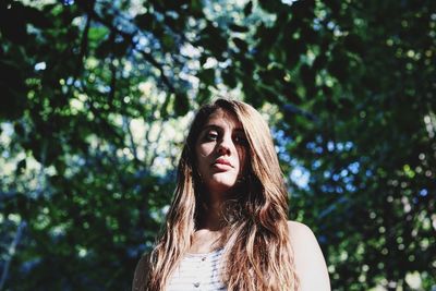 Low angle portrait of young woman against trees