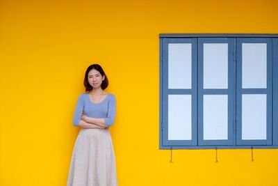 Portrait of young woman standing against yellow wall