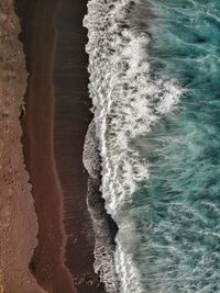 Top down view of blue ocean waves crashing into the black sand beach