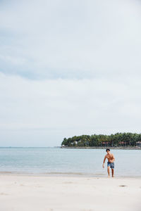 Rear view of woman standing at beach against sky