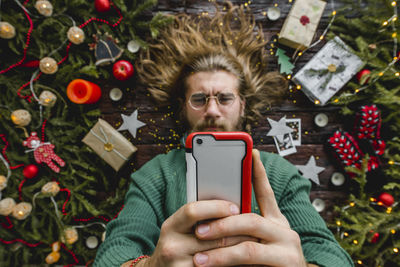 Midsection of man using mobile phone on christmas tree